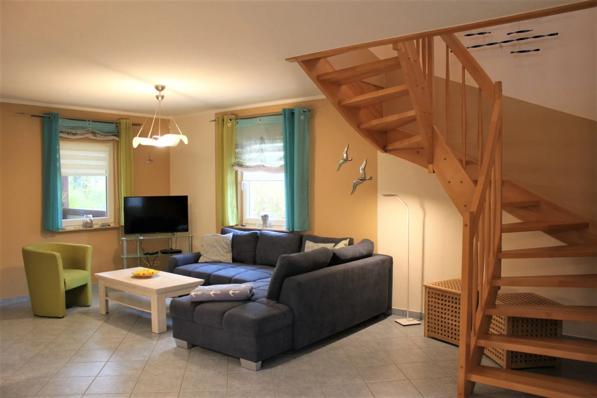 Wohnzimmer mit Eckcouch, Flachbildfernseher und offener Holztreppe